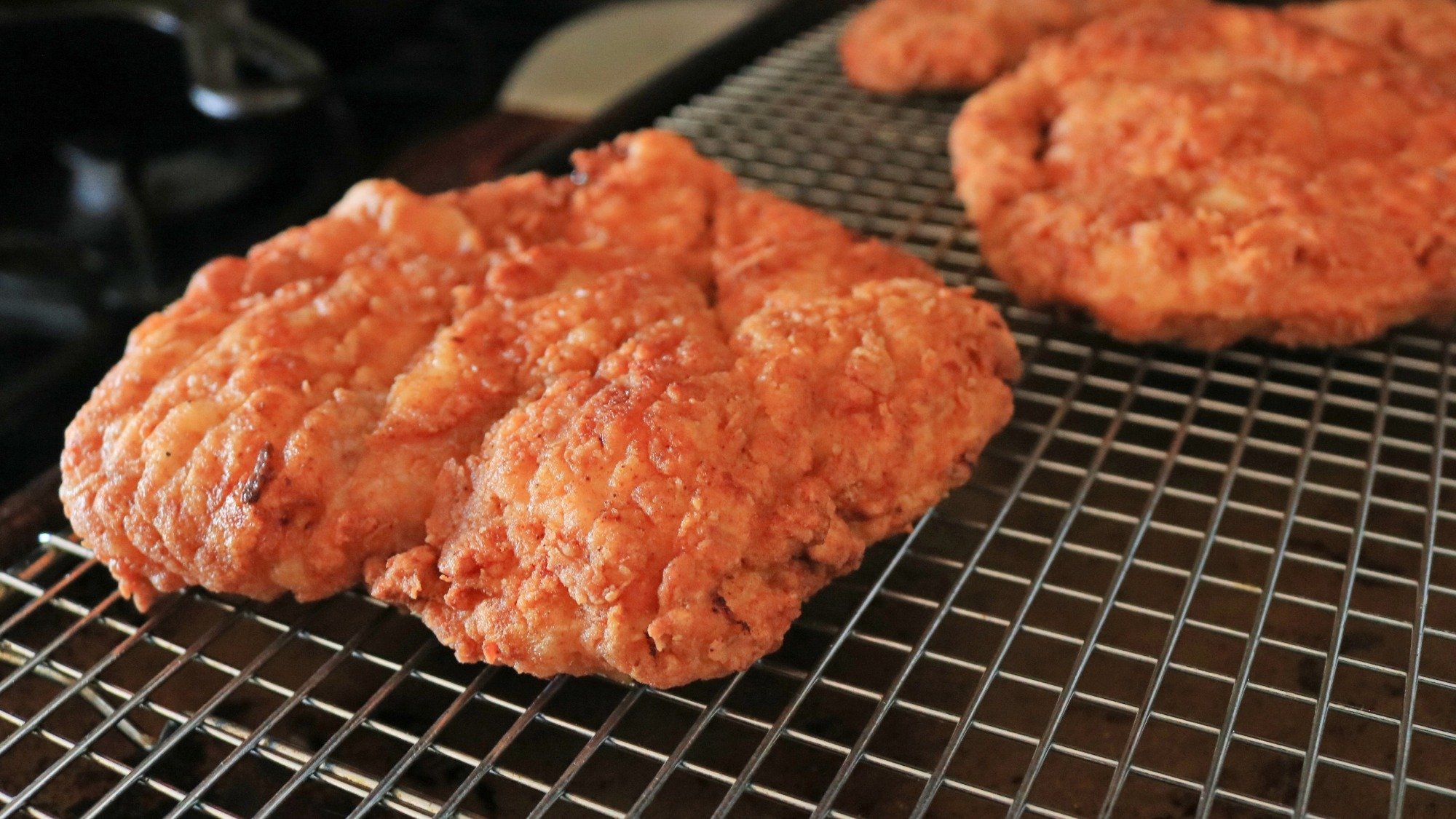 Two fried chicken cutlets on a wire rack.