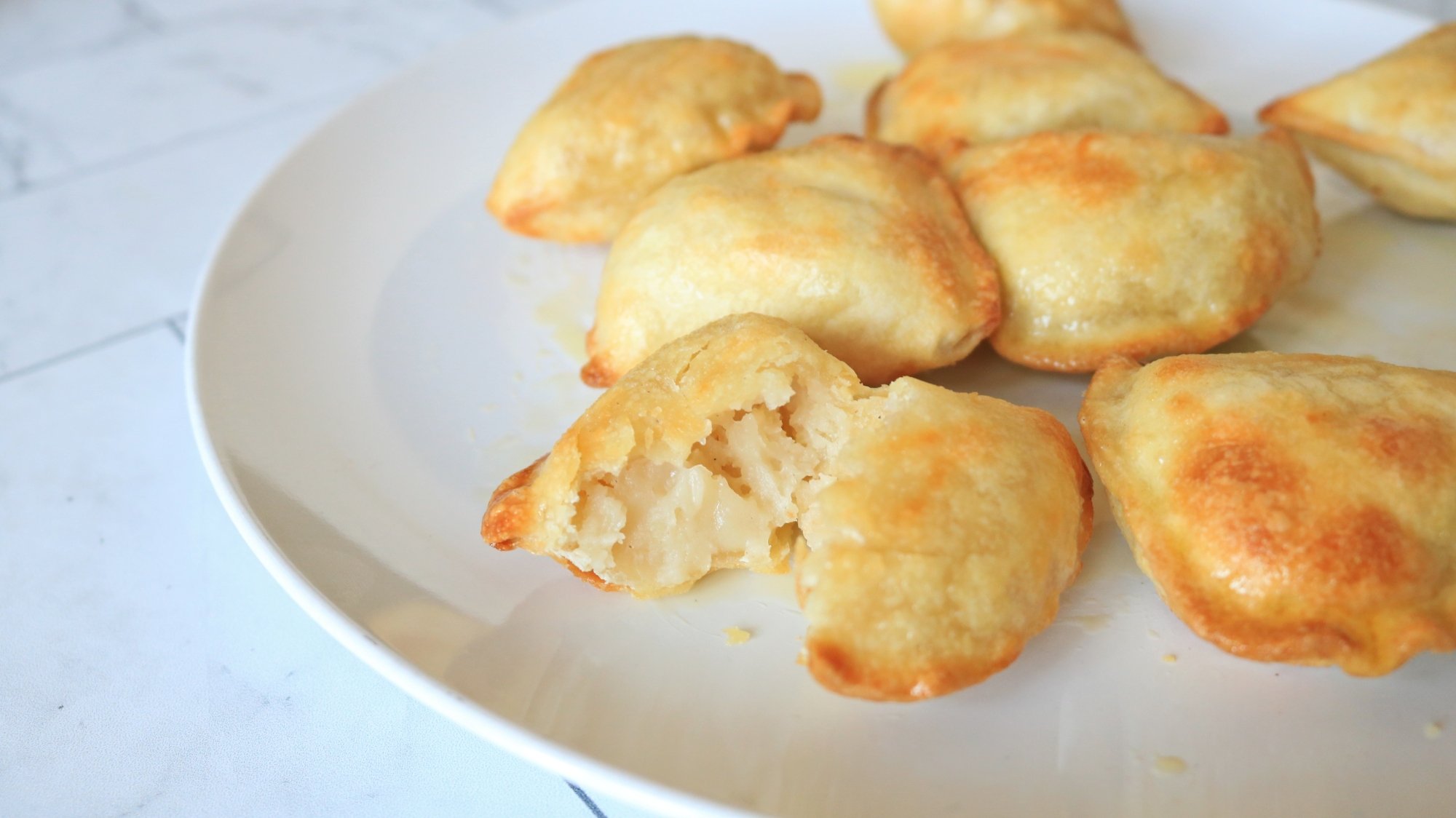 A plate of air-fried pierogies, with one broken open in front.